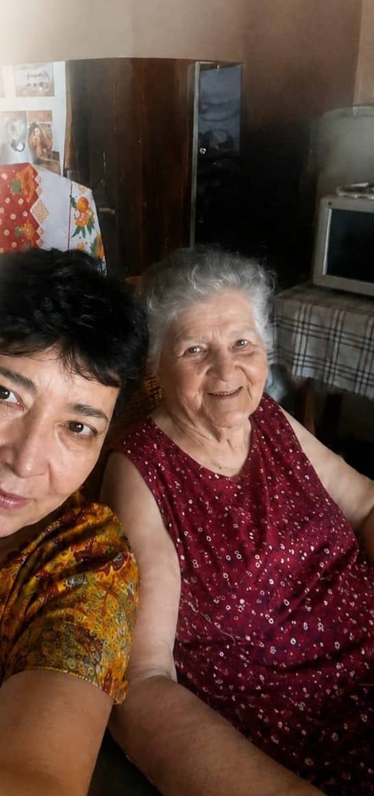 Norma, de blusa amarilla con flores, junto a su madre, Luisa Caballero, que sonríe con un vestido rojo de lunares. Están en el interior de una casa.