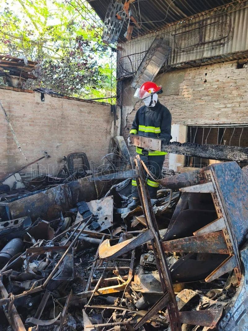 A firefighter in a red helmet among twisted metal, by day, in what was left of the house.