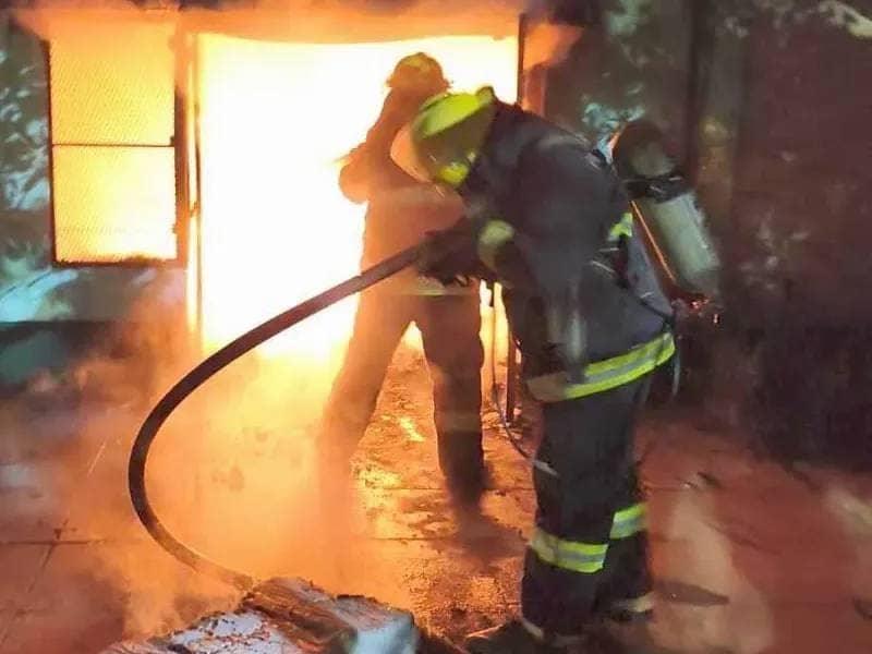 Two firefighters at the door of the house: one holds the hose and the other stands against the fire.